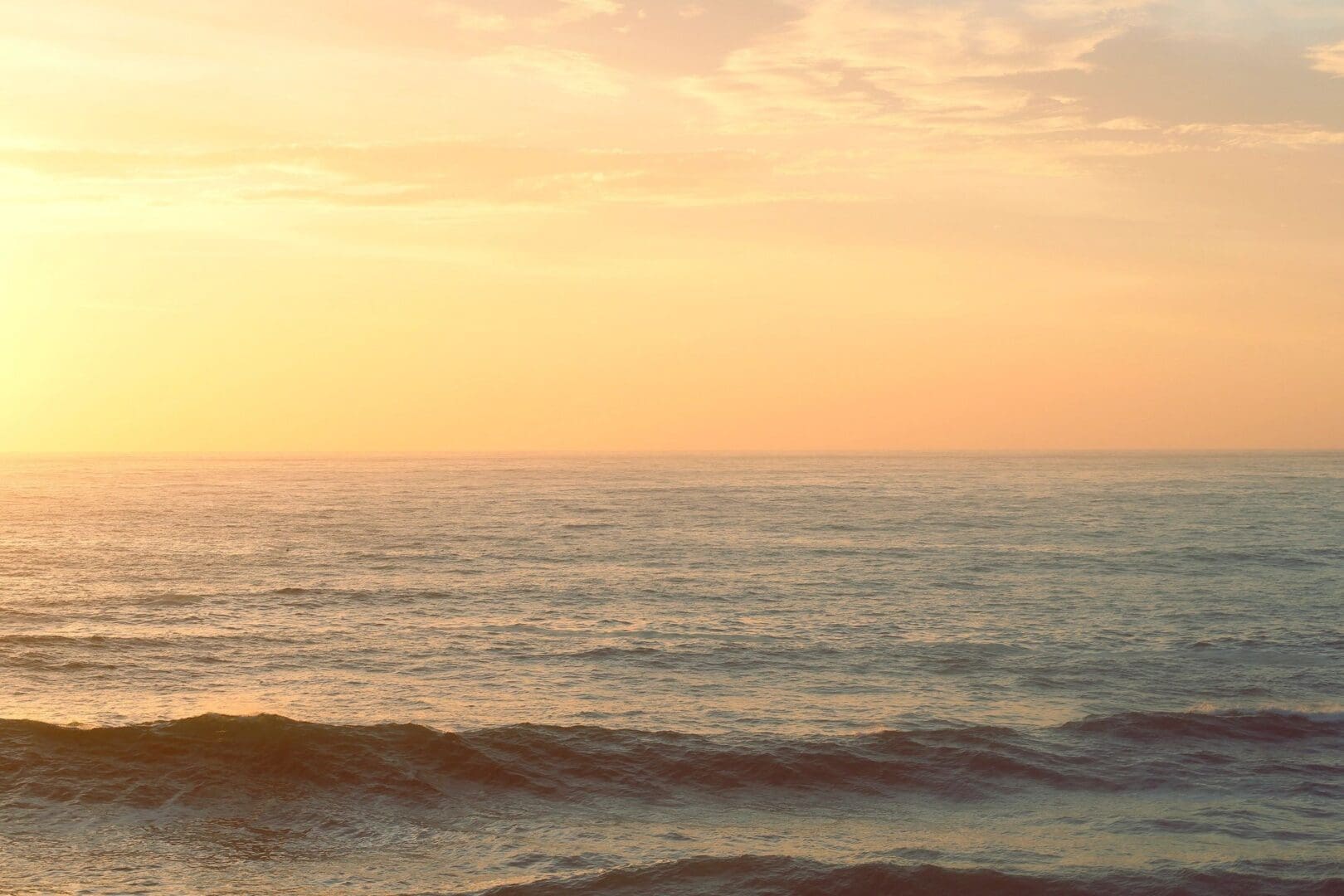 A sunset over the ocean with waves crashing on it.