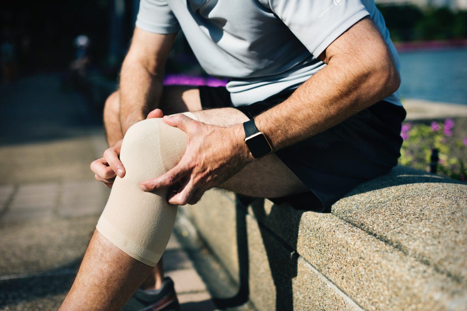 A man with his knee in plaster sitting on the side of a wall.